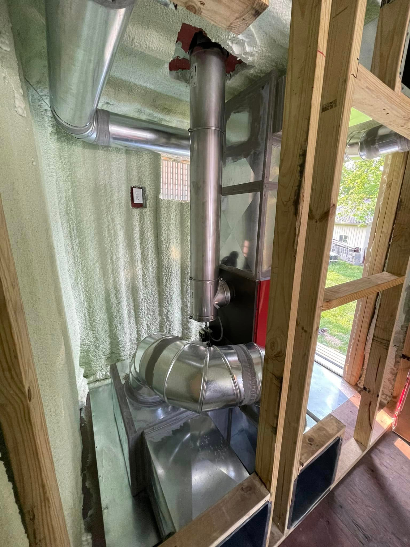 New galvanized ductwork and flue piping run through a spray-foam insulated mechanical room