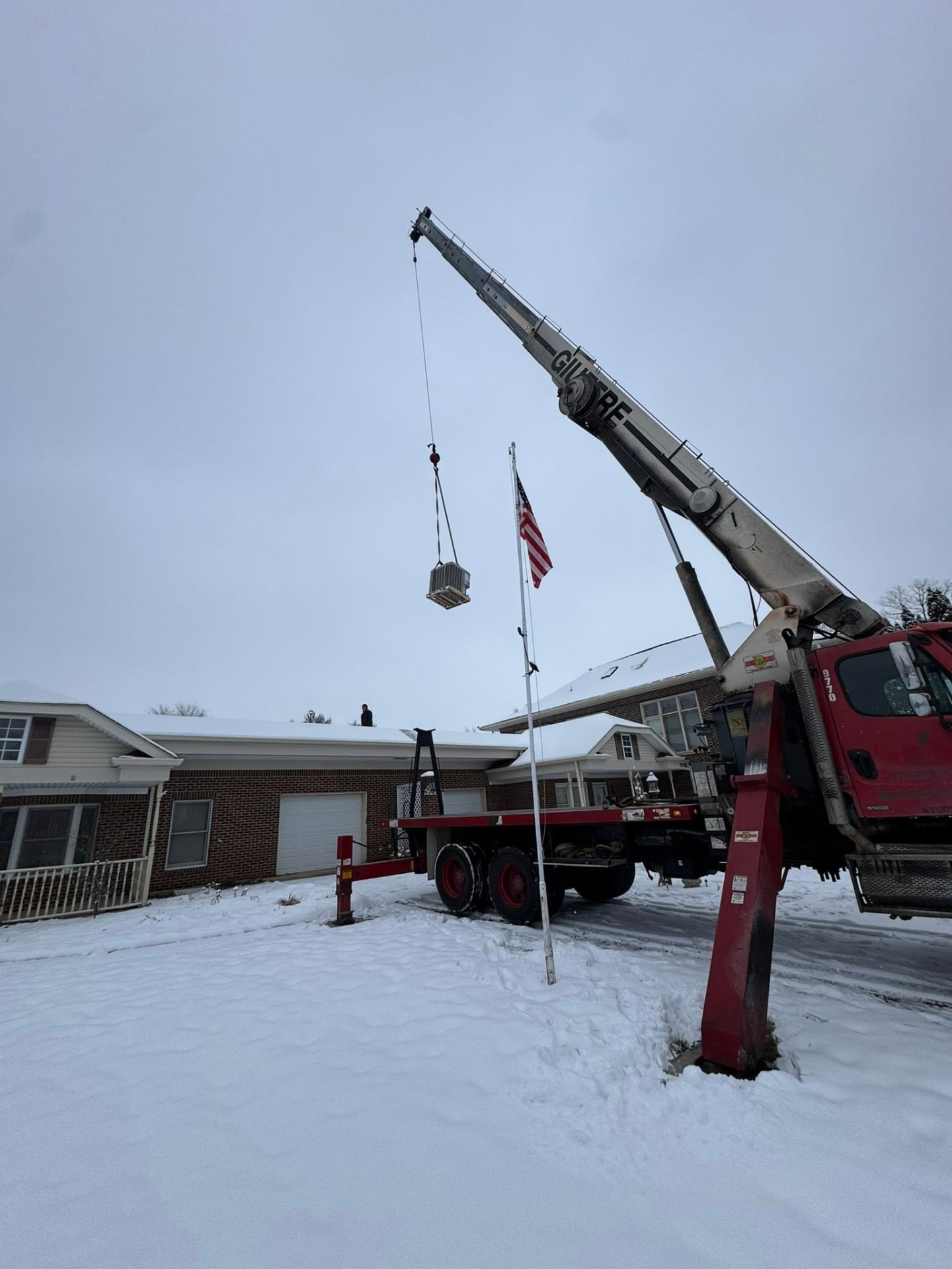 Boom truck setting HVAC equipment on a residential roof during an Indiana snowstorm